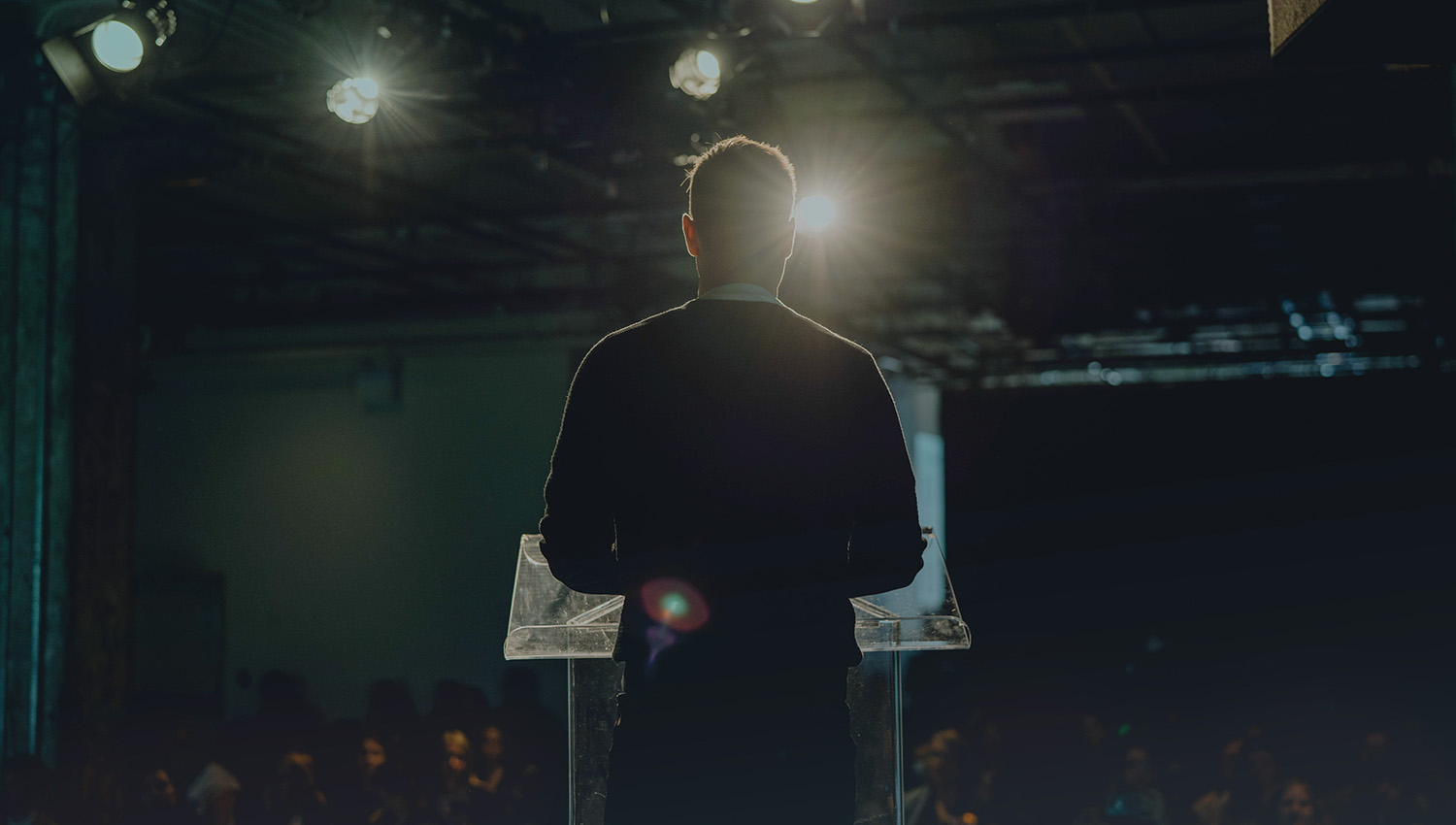 Speaker on stage addressing an audience at a business event.